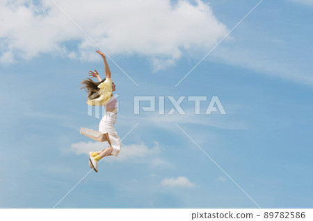 Girl during jump in the sky. Woman jumping through the air in front of beautiful cloudy sky. Carefree woman 89782586