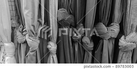 Curtain and fabric for drapery and interior decoration. Samples of fabrics in the store are hung vertically and tied in knots. Curtains in the showcase. Curtain monochrome black, gray and white color. Curtain and fabric for drapery and interior decoration. Samples of fabrics in the store are hung vertically and tied in knots. Curtains in the showcase. Curtain monochrome black, gray and white color. 89783003