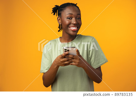 Happy smiling african american girl using her smartphone in yellow studio. Happy smiling african american girl using her smartphone in yellow studio. 89783135