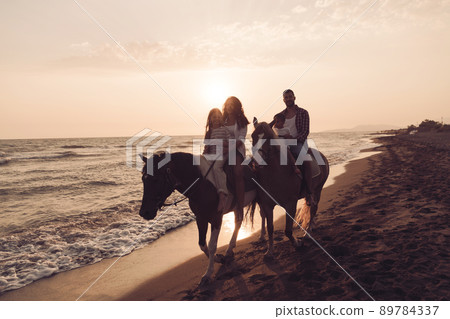 The family spends time with their children while riding horses together on a beautiful sandy beach on sunet. The family spends time with their children while riding horses together on a beautiful sandy beach on sunet. 89784337