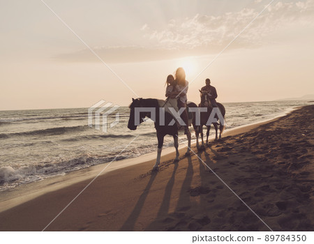 The family spends time with their children while riding horses together on a beautiful sandy beach on sunet. The family spends time with their children while riding horses together on a beautiful sandy beach on sunet. 89784350