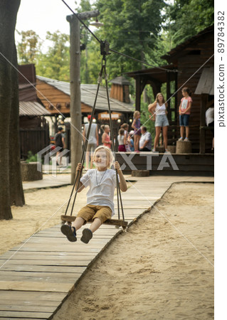 Happy boy on wooden swing and smiles. Carefree childhood. Boy has fun on the childrens playground. Happy boy on wooden swing and smiles. Carefree childhood. Boy has fun on the childrens playground. 89784382