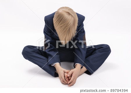 Boy in school uniform sits with head down and hands on his legs. Tired or sad blond schoolboy. Boy in school uniform sits with head down and hands on his legs. Tired or sad blond schoolboy. 89784394
