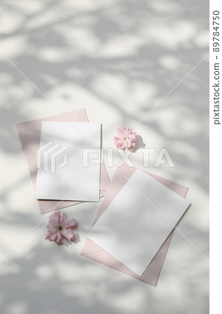 Wedding still life. Feminine spring breakfast scene. Pink Japanese cherry tree, sakura blossoms in sunlight. Blank greeting card, invitation. Blush pink envelopes. White dappled table background Wedding still life. Feminine spring breakfast scene. Pink Japanese cherry tree, sakura blossoms in sunlight. Blank greeting card, invitation. Blush pink envelopes. White dappled table background 89784750