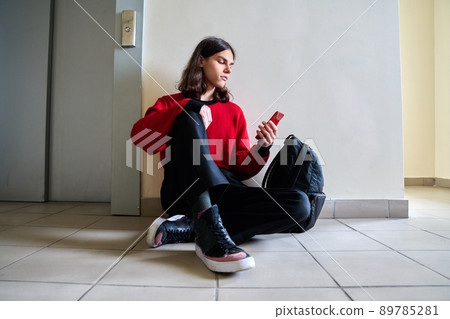 Teenage trendy male with smartphone backpack sitting on the floor 89785281