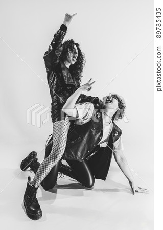 Studio shot of excited, astonished young boy and girl with bright makeup wearing black leather outfits moving on white background. Music, youth 89785435