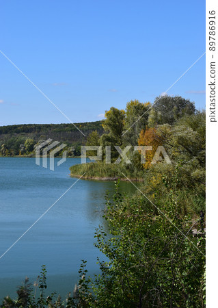 Forest lake in the autumn afternoon. Calm water with reflection of trees. 89786916