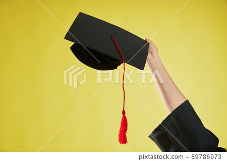 Front view of female hand raising, holding, showing mortarboard. Girl wearing graduate gown graduating from college, university, high school. Isolated on green background. 89786973