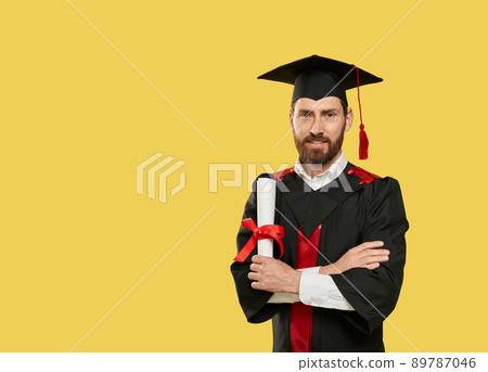 Front view of handsome male with beard graduating from unversity, college. Student getting bachelor, master degree, holding diploma. Isolated on yellow studio background. 89787046