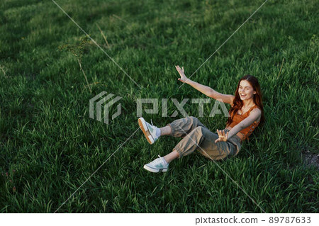 A young woman is playing in the park with us in the grass and falls to the ground smiling happily in the sunlight. Resting in nature, harmony with the body A young woman is playing in the park with us in the grass and falls to the ground smiling happily in the sunlight. Resting in nature, harmony with the body 89787633