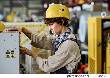 Side view of serious engineer in hardhat pressing start button on machine panel 89788422