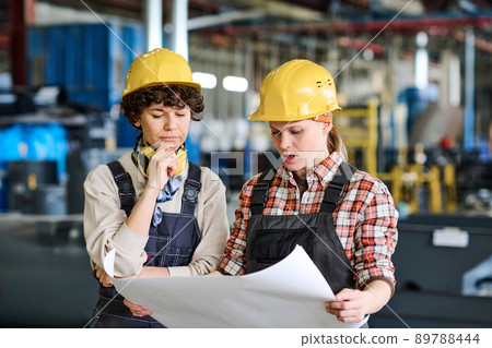 Pensive female engineer looking at sketch on blueprint held by colleague Pensive female engineer looking at sketch on blueprint held by colleague 89788444