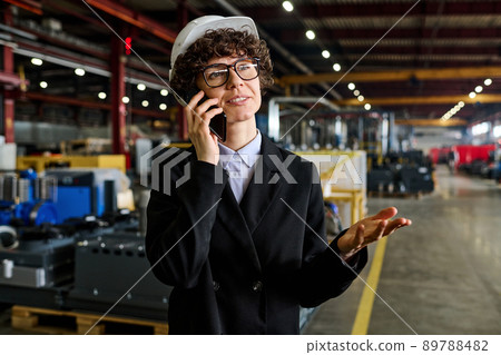 Confident manager in black suit and protective helmet talking on smartphone 89788482