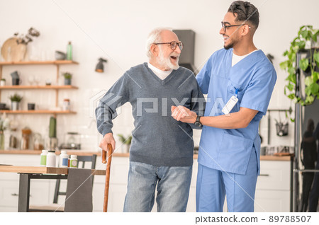 Patient leaning on the cane supported by a young nurse 89788507