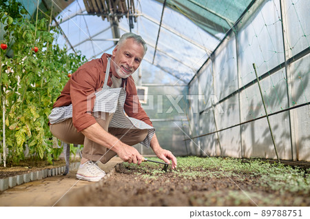 Man looking at camera crouched near greenhouse garden 89788751