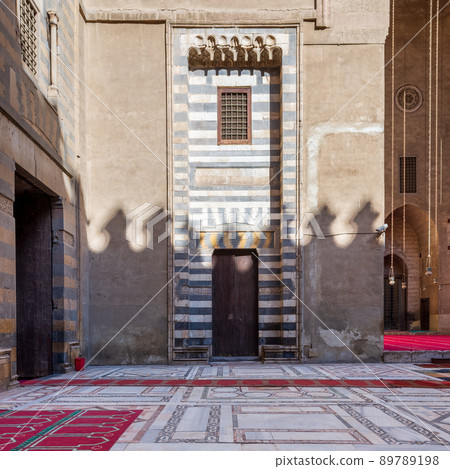 Wall with striped black and white marble decorations, wooden grunge door and window, Sultan Hassan mosque, Cairo, Egypt 89789198