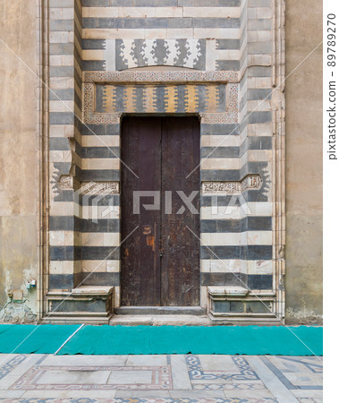 Wooden aged door surrounded by striped black and white marble decorations and stone wall, Sultan Hassan Mosque, Cairo, Egypt Wooden aged door surrounded by striped black and white marble decorations and stone wall, Sultan Hassan Mosque, Cairo, Egypt 89789270