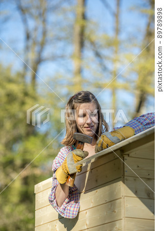 DIY concept - young woman holding a hammer working on a wooden playhouse DIY concept - young woman holding a hammer working on a wooden playhouse 89789898