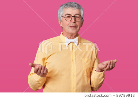 Elderly male does not know what kind of emotion to express, raises his palms up. Old man with yellow shirt and black rounded spectacles feels some confusion. Senior does not understand what happened. 89789918