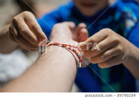Boy tying a string made bracelet to his fathers wrist 89790284