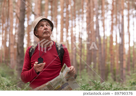 Close up shot of eldery man hiking and looking up at sky, using map and compass for direction for trip in forest, traveling around world, having adventure in wood, enjoying his active vacation. 89790376