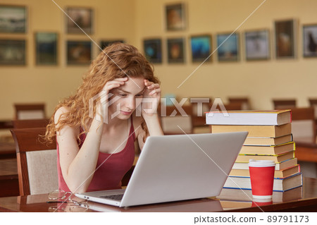 Task, test, learning and education concept. Intelligent, reader girl wearing casually sitting at desk in reading room in front of laptop, keeps hands on forehead, preparing for important exam. Task, test, learning and education concept. Intelligent, reader girl wearing casually sitting at desk in reading room in front of laptop, keeps hands on forehead, preparing for important exam. 89791173
