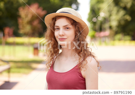 Closeup portrait of smiling beautiful girl posing in fresh air, having pleasant facial expression, standing around numerous trees and green, being in good mood. People and urban life concept. Closeup portrait of smiling beautiful girl posing in fresh air, having pleasant facial expression, standing around numerous trees and green, being in good mood. People and urban life concept. 89791190
