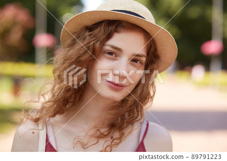 Close up portrait of charming curly haired adorable girl having natural look, being happy to rest at local green park, being in good mood, looking directly at camera. People and emotions concept. Close up portrait of charming curly haired adorable girl having natural look, being happy to rest at local green park, being in good mood, looking directly at camera. People and emotions concept. 89791223