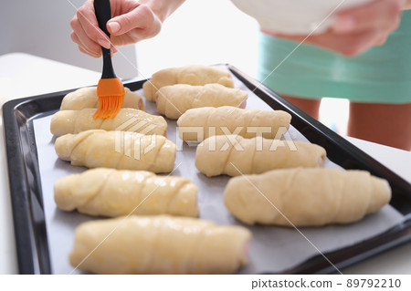 Woman prepares croissants and brush dough with egg yolk 89792210