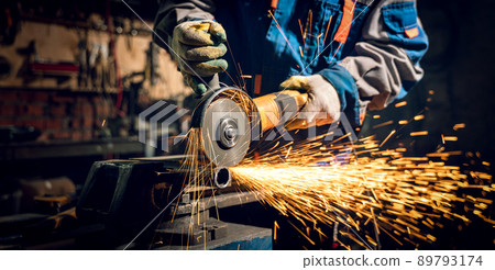 Locksmith in special clothes and goggles works in production. Metal processing with angle grinder. Sparks in metalworking 89793174