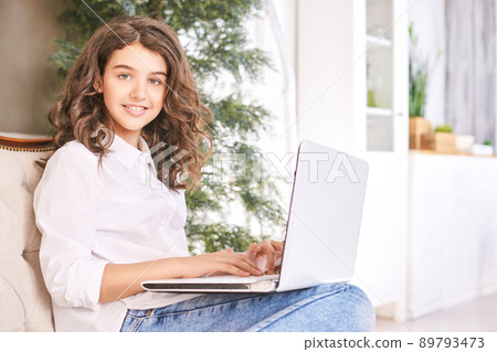 Female teenager using laptop on sofa. School online lessons Female teenager using laptop on sofa. School online lessons 89793473