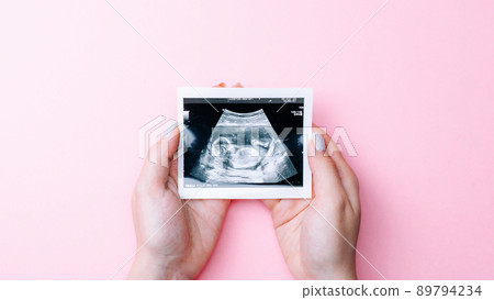 Ultrasound picture pregnant baby photo. Woman hands holding ultrasound pregnancy image on pink background. Concept of pregnancy, maternity, expectation for baby birth. Ultrasound picture pregnant baby photo. Woman hands holding ultrasound pregnancy image on pink background. Concept of pregnancy, maternity, expectation for baby birth. 89794234