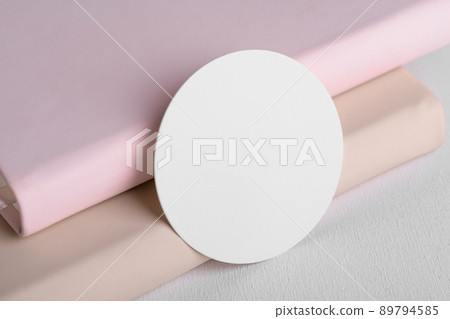 Round white gift tag mockup on beige and pink book background. Blank paper circular price sticker tag mockup 89794585
