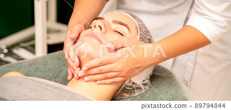 Facial treatment massage. Beautiful young caucasian woman with perfect skin receiving face and neck massage at a beauty spa 89794844