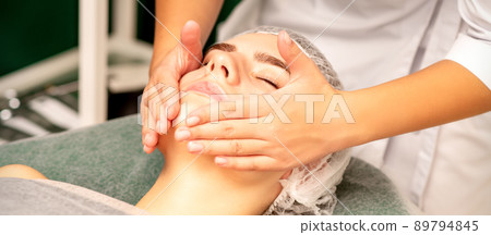 Facial treatment massage. Beautiful young caucasian woman with perfect skin receiving face and neck massage at a beauty spa 89794845