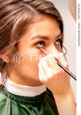 The makeup artist applies a concealer under the eyes using a makeup brush The makeup artist applies a concealer under the eyes using a makeup brush 89794854