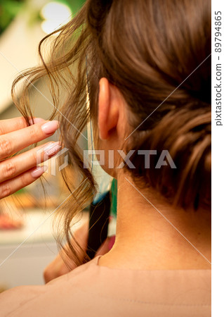 Professional hairdresser styling and fixing with hairspray long woman curly hair in a beauty salon 89794865