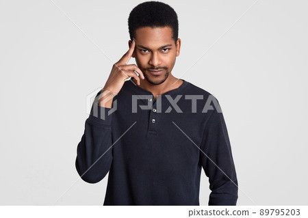 Photo of serious African American man keeps fore finger on temple, looks with confidence at camera, being deep in thoughts, remember important information, isolated over white studio background Photo of serious African American man keeps fore finger on temple, looks with confidence at camera, being deep in thoughts, remember important information, isolated over white studio background 89795203