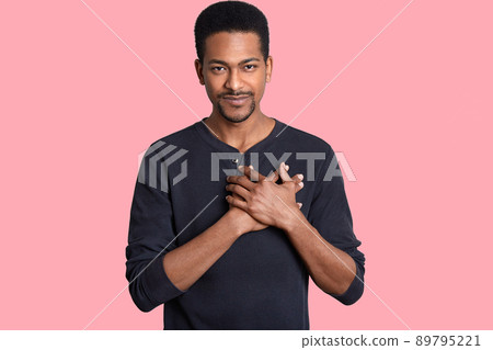 Horizontal shot of impressed touched man holds hands on chest, expresses thankfullness, hears heart piercing words, dressed in casual jumper, isolated over pink background. People and gratitude 89795221