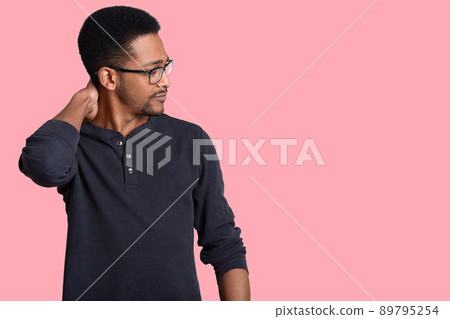 Sideways shot of serious Afro American male manager scratches neck, concentrated aside, wears optical glasses and casual sweater, isolated over pink background with copy space for your promotion Sideways shot of serious Afro American male manager scratches neck, concentrated aside, wears optical glasses and casual sweater, isolated over pink background with copy space for your promotion 89795254