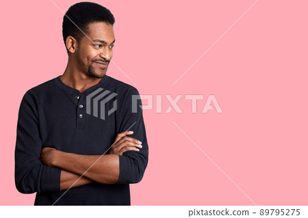 Portrait of confident charismatic young handsome African American male in black casual shirt with hands crossed on chest. Guy looks smiling aside. Attractive man with short hairstyle and beard poses. 89795275