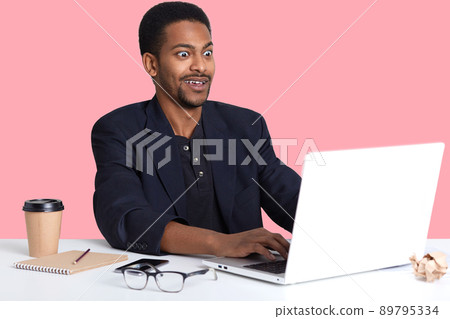 Indoor portrait of young surprised black male sitting at table, works with lap top, looks with astonisment on monitor. Handsome guy typing on keyboard, expreses shock with face. Online working concept Indoor portrait of young surprised black male sitting at table, works with lap top, looks with astonisment on monitor. Handsome guy typing on keyboard, expreses shock with face. Online working concept 89795334