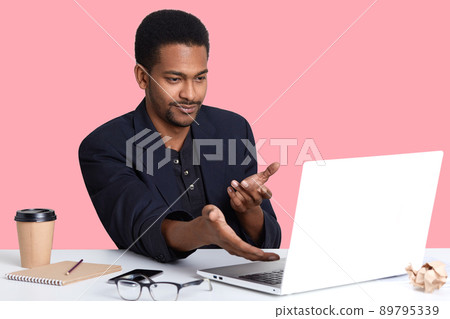 Perplexed young business man in black jacket, shows with both hands on lap top monitor, sees arror, do not understend what happened, uses wireless Internet, working online, earns money in office. Perplexed young business man in black jacket, shows with both hands on lap top monitor, sees arror, do not understend what happened, uses wireless Internet, working online, earns money in office. 89795339