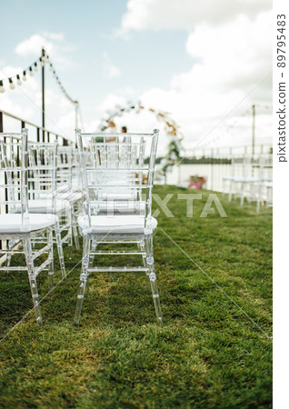 Round arch for a wedding ceremony by the river. White glass chairs stand for guests Round arch for a wedding ceremony by the river. White glass chairs stand for guests 89795483