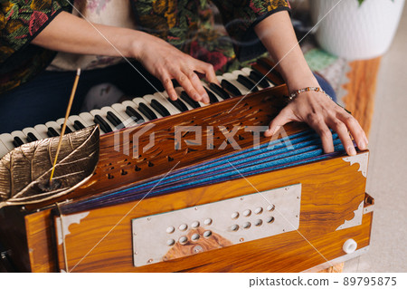Hands of a woman sitting on the floor and playing the harmonium during the practice of kundalini yoga 89795875