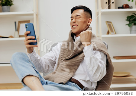 handsome man sitting in a chair in a room with phone on his lap Lifestyle handsome man sitting in a chair in a room with phone on his lap Lifestyle 89796088