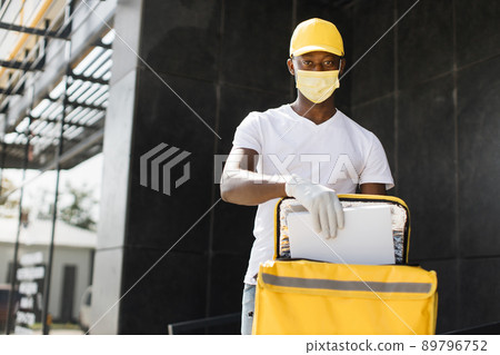 Delivery man carrying yellow thermal backpack and cardboard box while waiting to give order 89796752