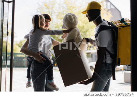 African courier deliver to young attractive female and her daughter a parcel with teddy bear African courier deliver to young attractive female and her daughter a parcel with teddy bear 89796754