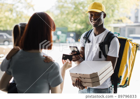 Young smiling woman with a girl at the door, pay by card for online order. Young smiling woman with a girl at the door, pay by card for online order. 89796833