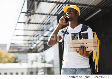 Young African American courier, pizza and coffee delivery man with thermal backpack and phone. Young African American courier, pizza and coffee delivery man with thermal backpack and phone. 89796857